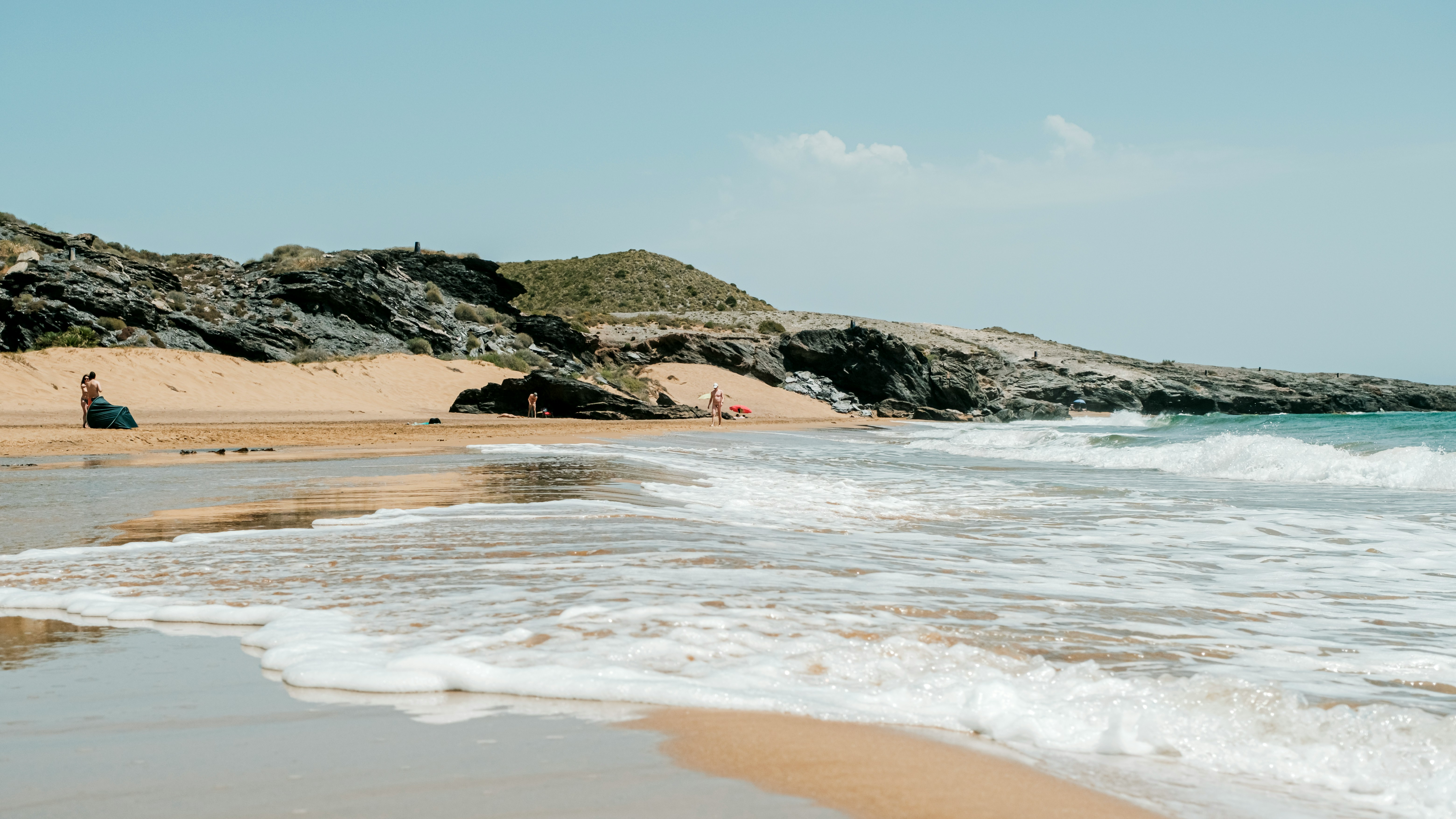 Waves washing onto a quiet sandy beach with low rocky hills along the Murcia coastline, showing the wilder side of the region’s coastal day trips.